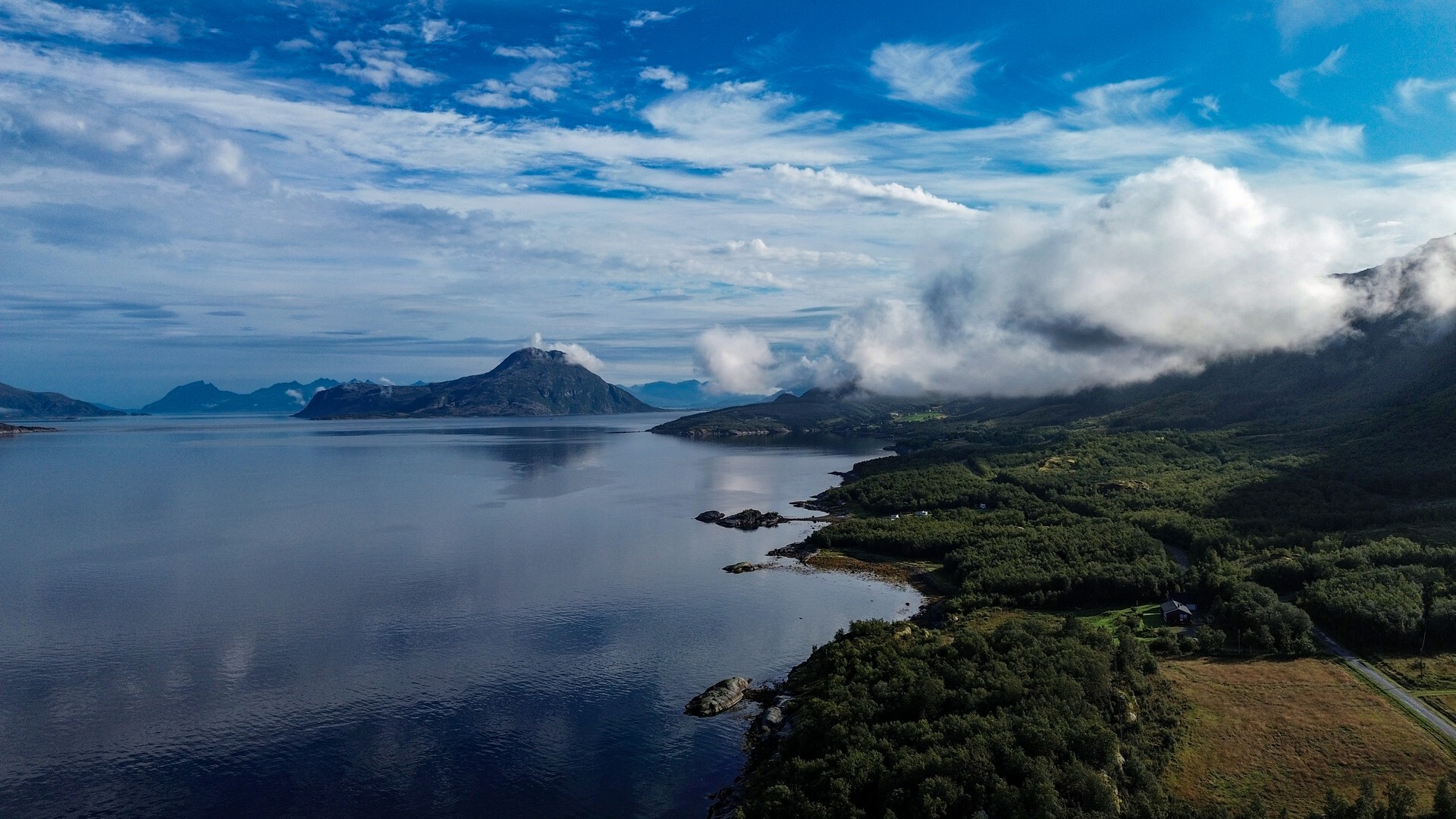 Fiord i zalesiony brzeg pod kłębiastymi chmurami – krajobraz Helgelandu z lotu ptaka